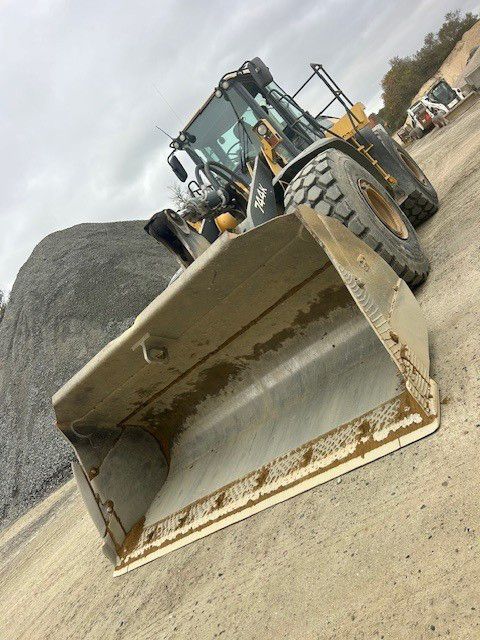 Wheel loader with a large bucket parked in front of a gravel pile on a construction site.