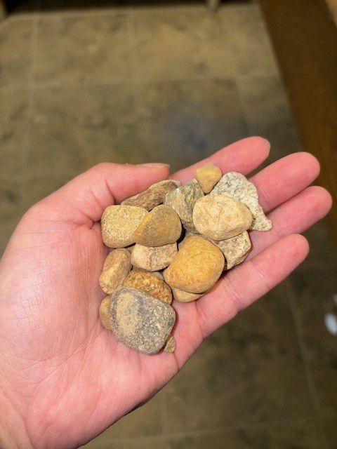 Hand holding a pile of smooth, light-brown river rocks.