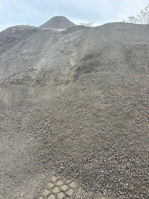 Pile of gravel and small rocks, with a small hill in the background. Gray tones.