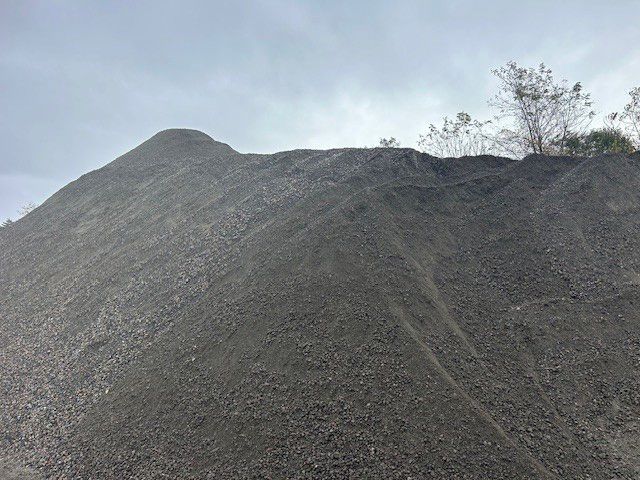 Large pile of gray gravel against a cloudy sky, with a few small trees on top.