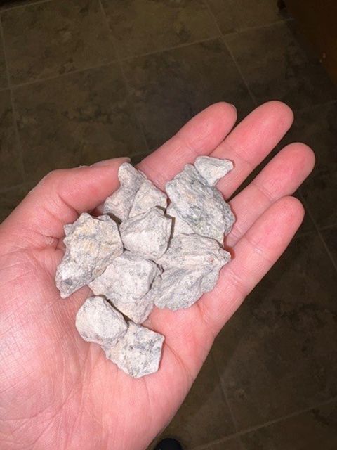 Hand holding a pile of light-colored, irregularly shaped rocks, on a tiled floor.
