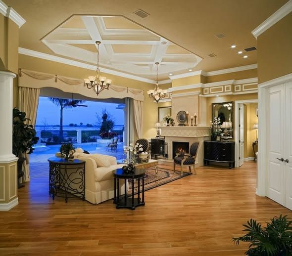 Living room with wood floor, fireplace, and view of a pool. Beige walls, chandeliers, and patterned ceiling.