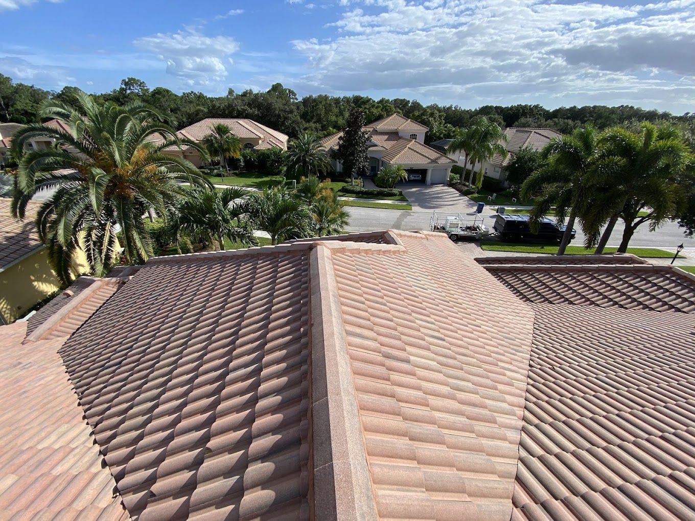 Brown tile roof with surrounding trees and houses on a sunny day.