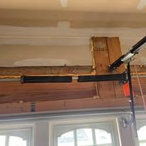 A close-up of a broken garage door torsion spring mounted on a horizontal bar above a garage door frame.