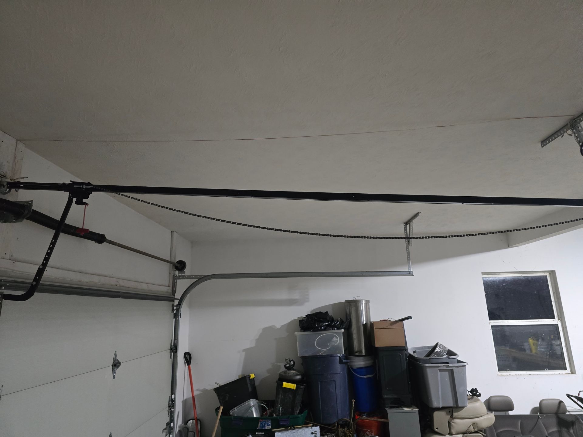 A garage ceiling showing a garage door opener rail and storage clutter in the background.