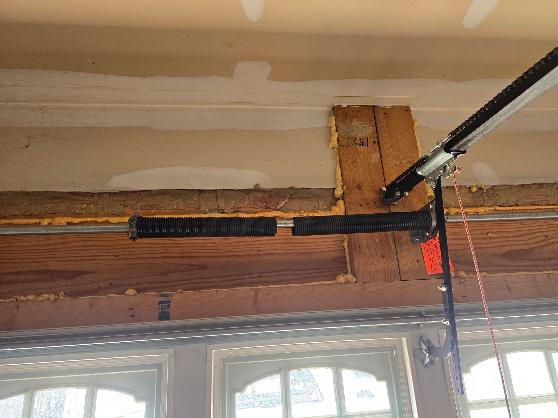 A garage door torsion spring is broken, showing a clear gap between the two segments on the horizontal metal shaft.