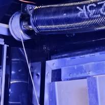 A heavy-duty metal torsion spring mounted above a garage door, with a lift cable attached to the side winding drum.