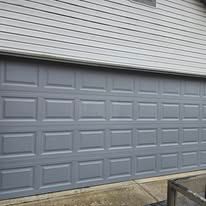 A gray multi-panel garage door installed under light-colored horizontal siding.