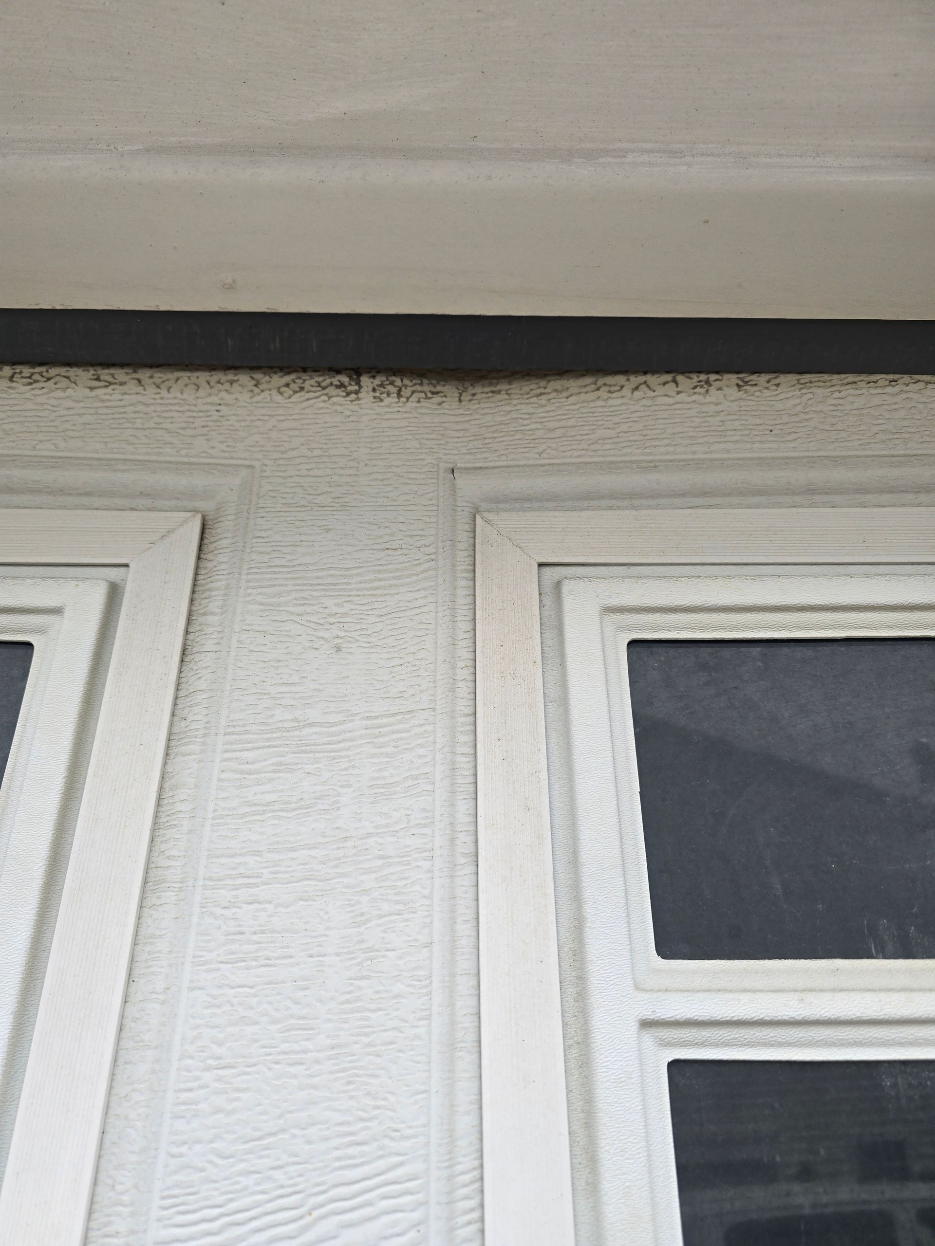 A close-up view of a white, textured exterior wall between two window frames, with a dark horizontal trim above.