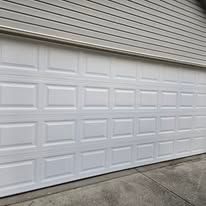 A white, multi-panel garage door installed on a house with light grey horizontal siding.