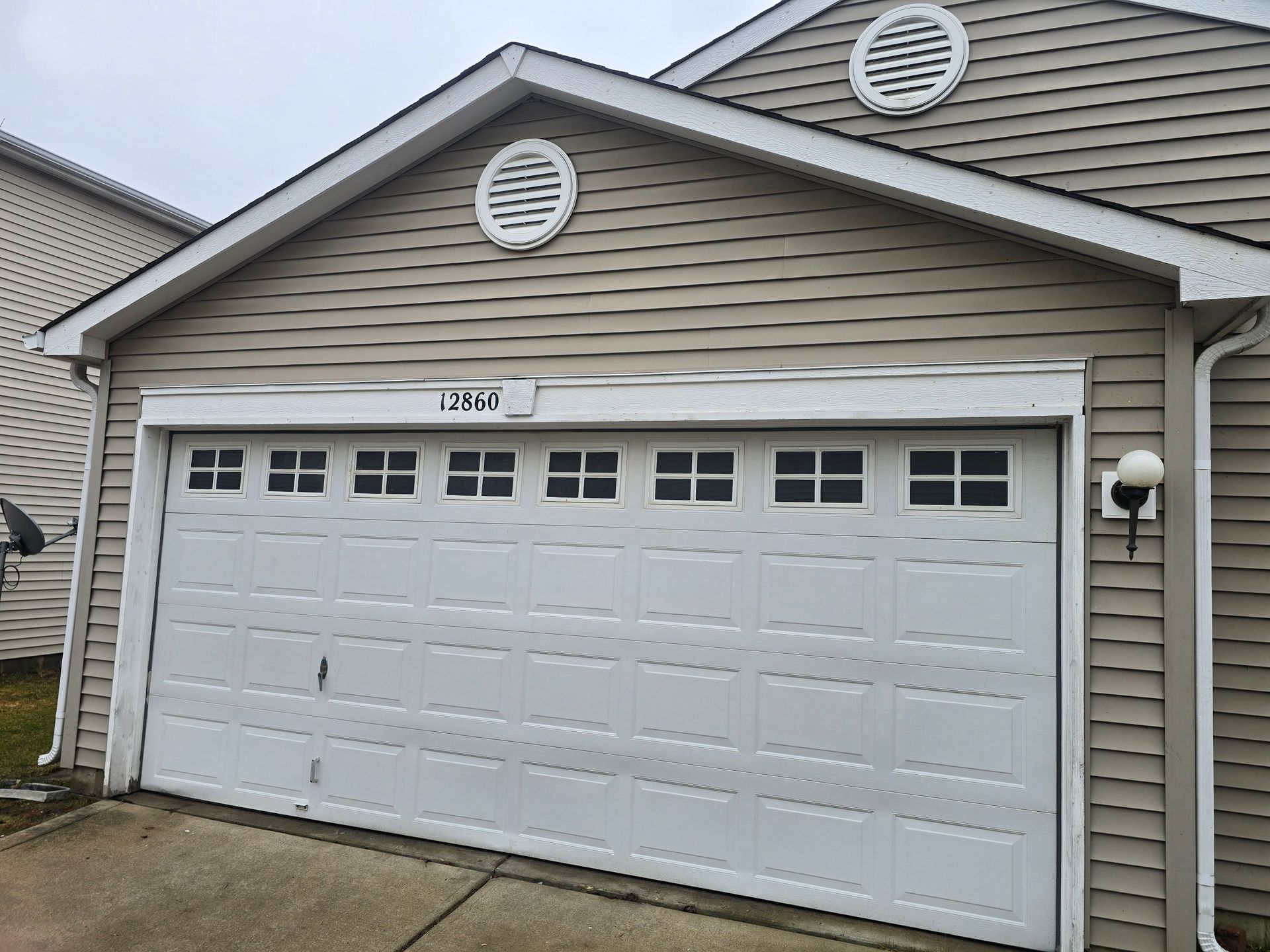 Beige suburban home with a white, windowed two-car garage door and round vents in the gable.
