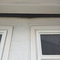 A close-up view of the white exterior wall and frame of a garage door, showing a thin gap beneath the header trim.