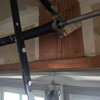 A close-up view of garage door hardware, showing a metal spring, horizontal torsion bar, and a vertical support bracket.