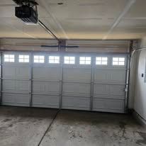 A closed white garage door with a row of small windows near the top, seen from inside a concrete-floored garage.