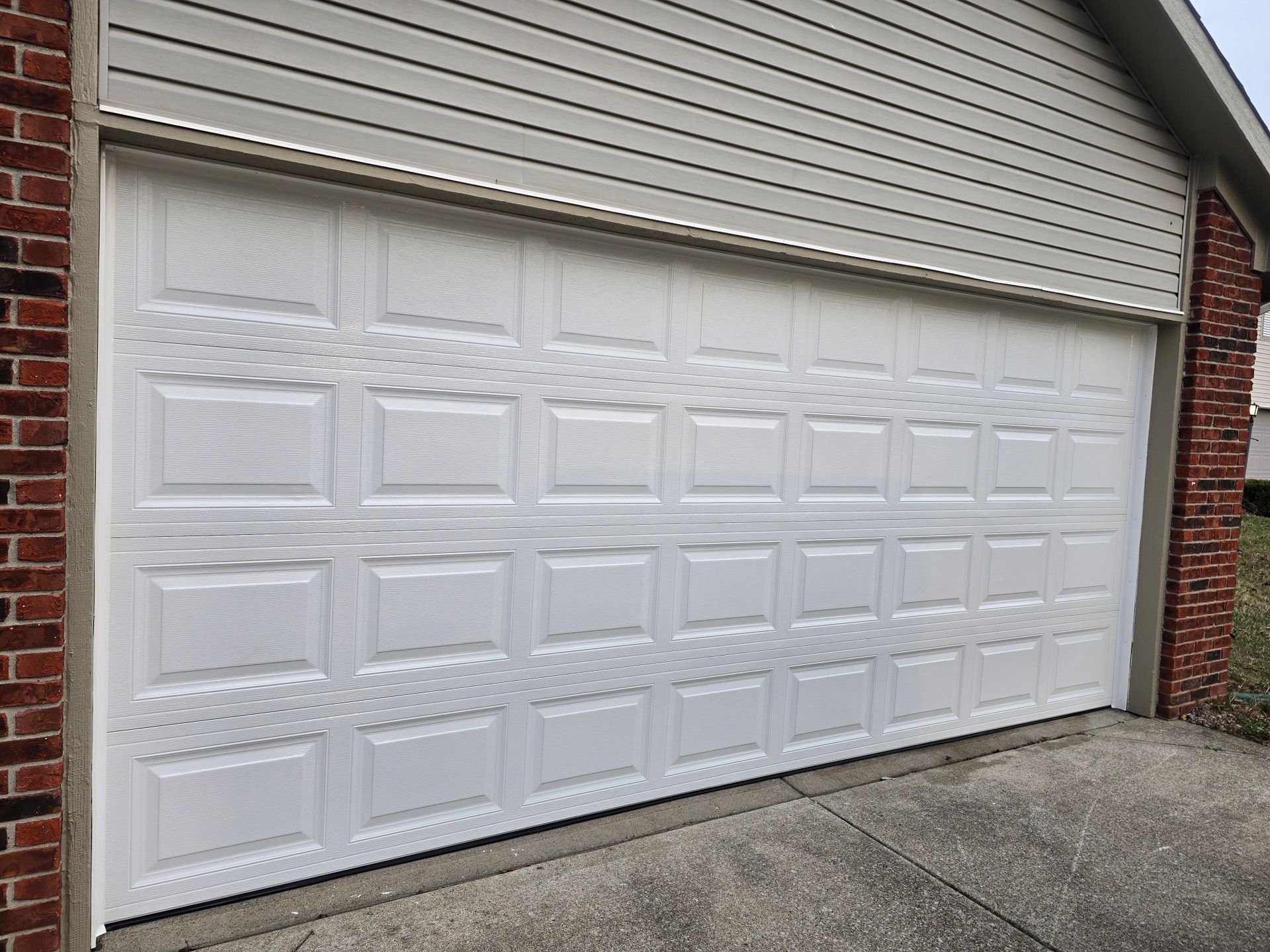 A white, multi-panel residential garage door framed by brick walls on the sides and light gray siding above.