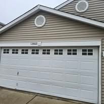 A white two-car garage door with windows on a beige house, featuring a house number label above the door.