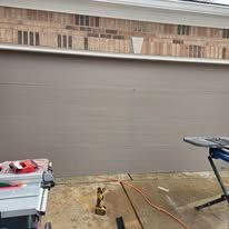 A tan garage door is closed above a concrete driveway with work tools positioned on stands in the foreground.