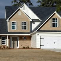 A two-story suburban house with beige siding, a brick lower level, a white garage, and a dark shingled roof.
