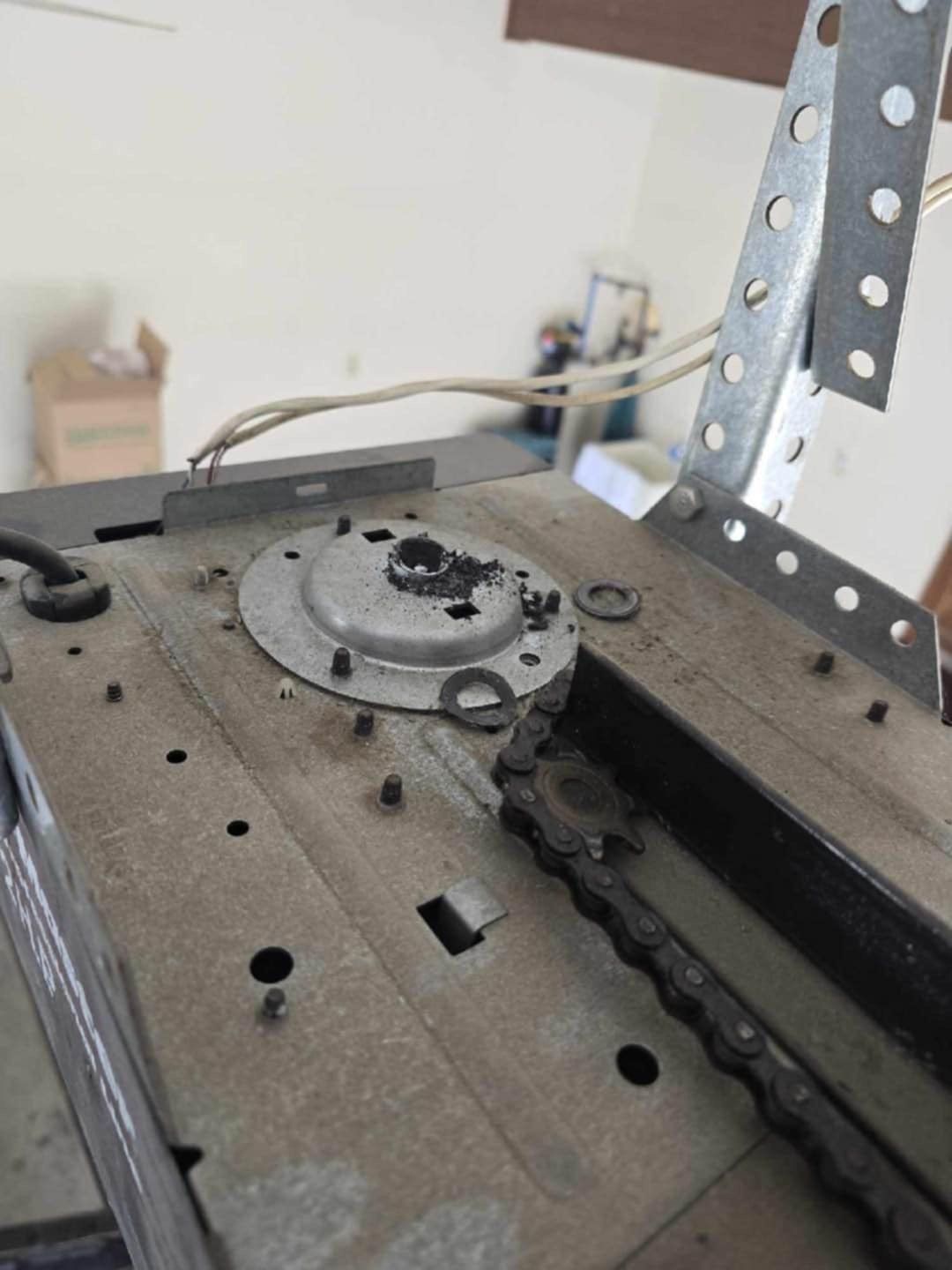 Close-up of a damaged garage door opener motor assembly, showing a broken drive gear with black plastic debris.
