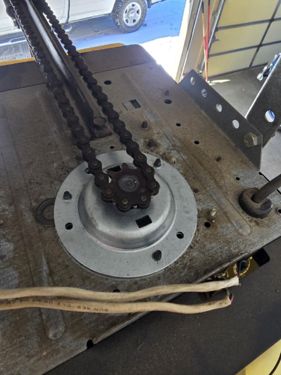 Close-up of a garage door opener motor, showing the metal chain attached to the center drive sprocket.