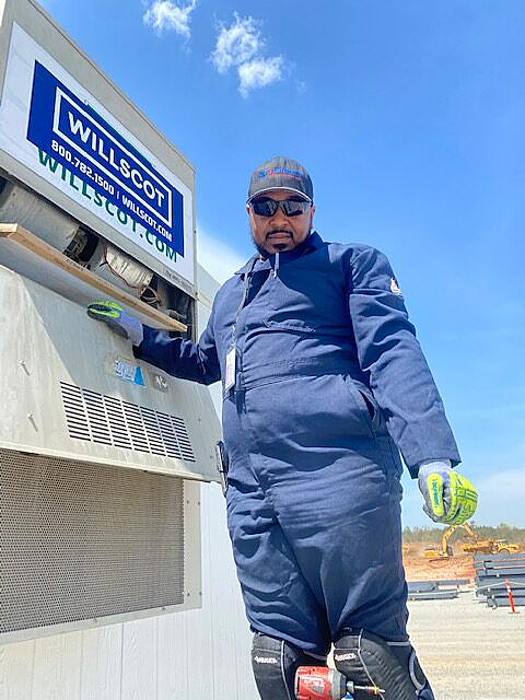 a man in a blue jumpsuit is standing in front of a willscott machine .