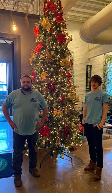 two men are standing in front of a christmas tree .