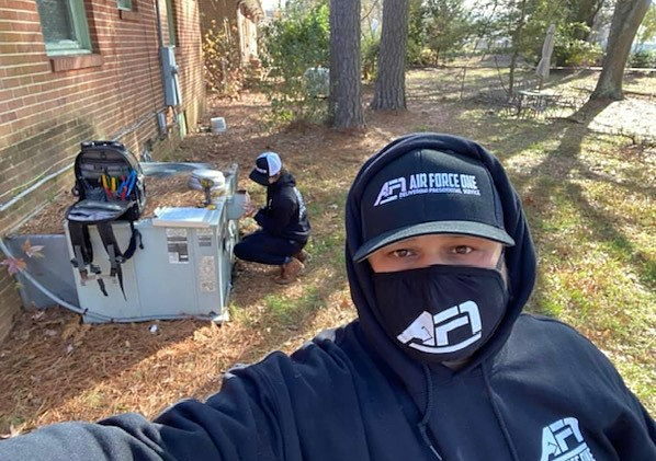 a man wearing a mask and a hat is working on an air conditioner .