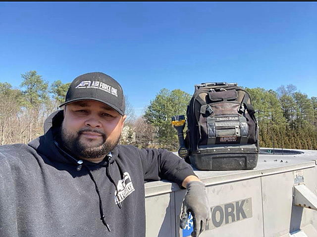 a man wearing a hat and a black hoodie is standing next to a tool bag .