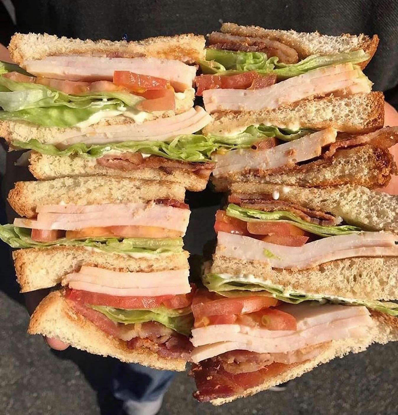 A person holding two halves of a large club sandwich, showing layers of turkey, bacon, lettuce, and tomato on toasted bread.
