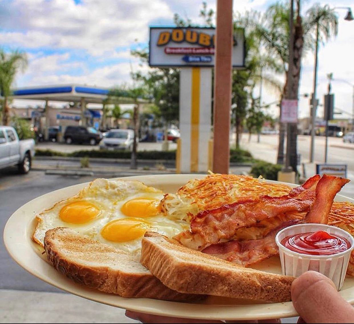 Plate of breakfast food: eggs, bacon, hash browns, toast, and ketchup in front of a diner.