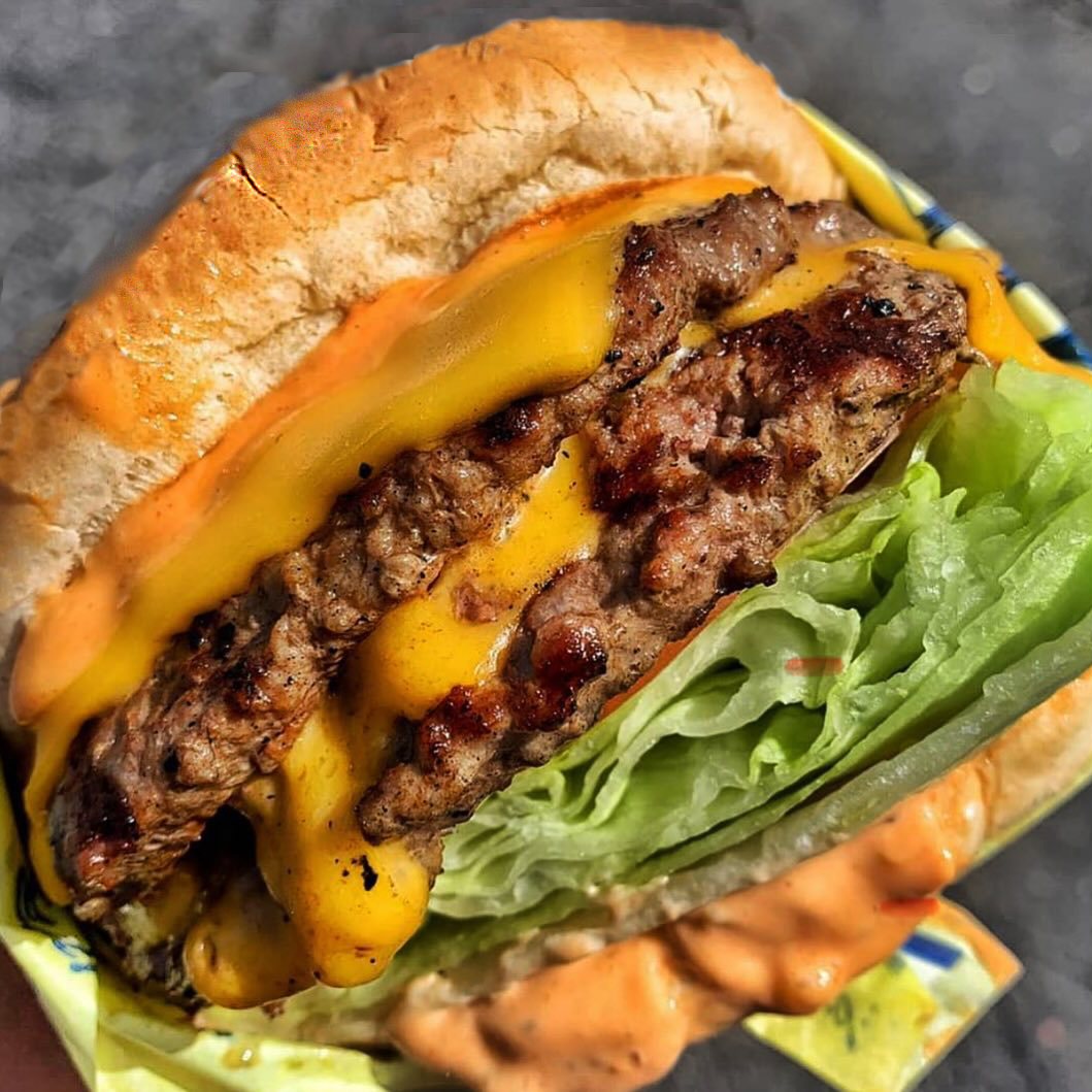 Double cheeseburger with melted cheese, lettuce, and sauce, on a sesame seed bun.