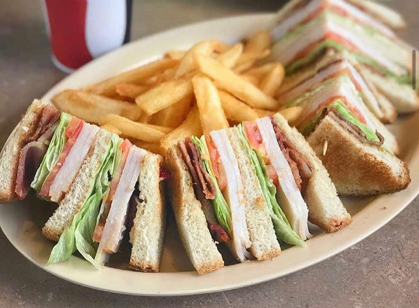 Club sandwiches and french fries on a plate. The sandwiches have turkey, bacon, lettuce, and tomato.