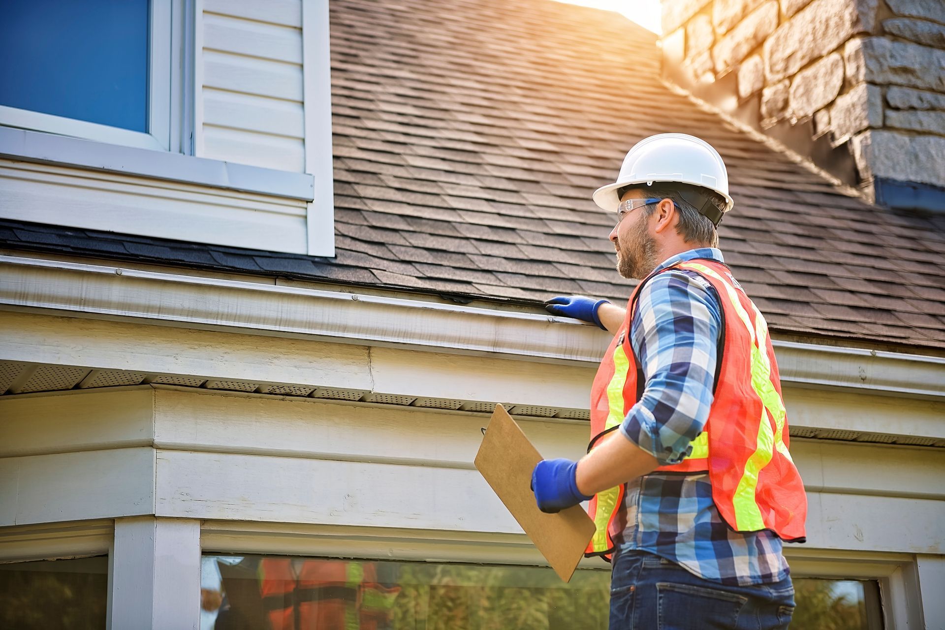 Home inspector in hard hat and safety vest examining house exterior with clipboard