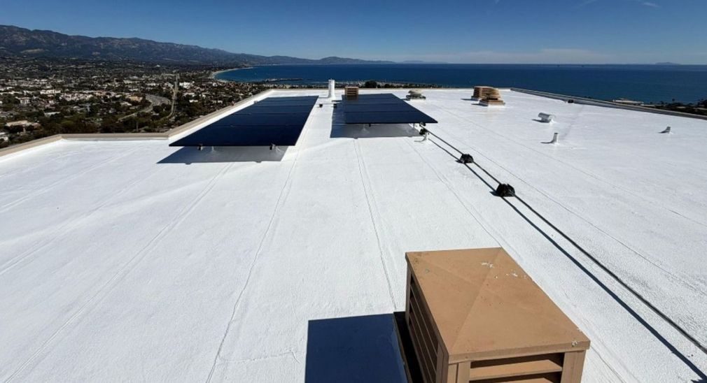 White rooftop with skylights, vents, and a coastal city and bay view in the distance