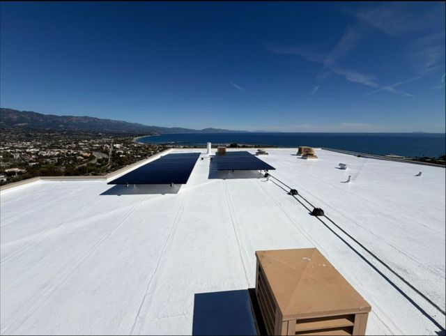 Flat white rooftop with solar panels overlooking a coastal town and blue sea under a clear sky