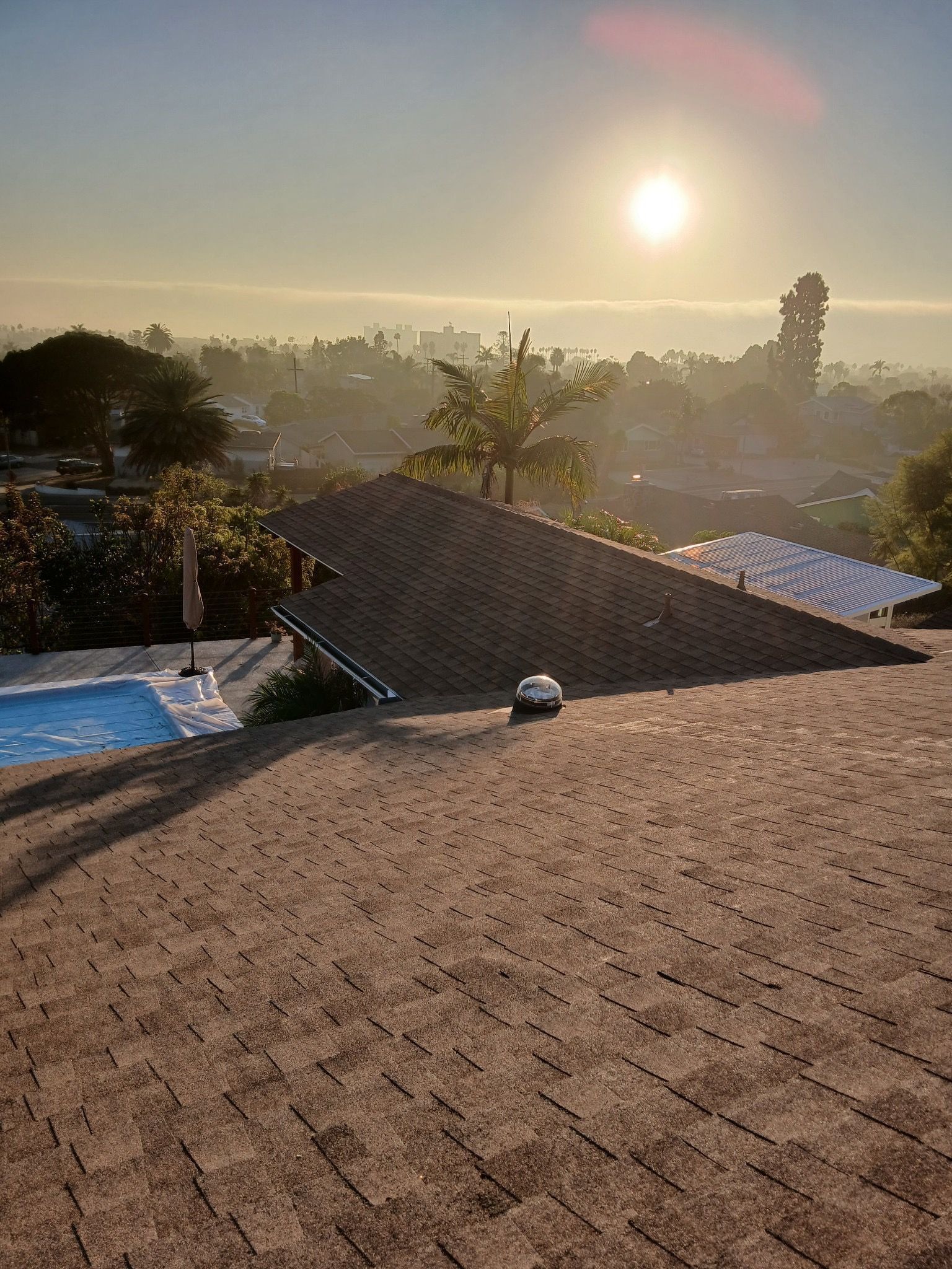Sunrise over misty rooftops and trees, with a sloped roof in the foreground