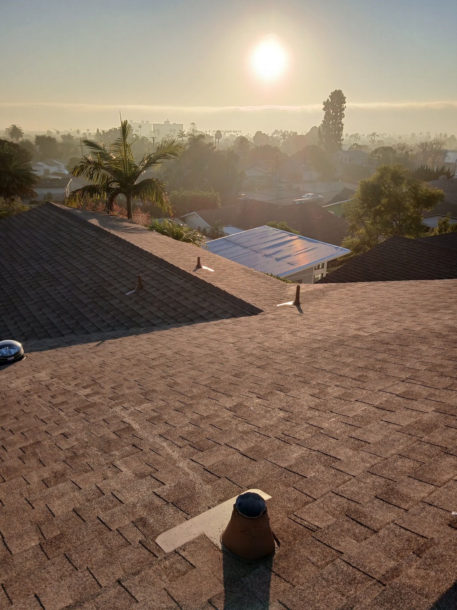 Sunrise over tiled rooftops and trees, with a hazy cityscape in the distance.