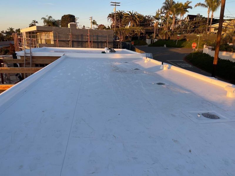 White rooftop at sunset with vents, beside a fenced tennis court and palm trees