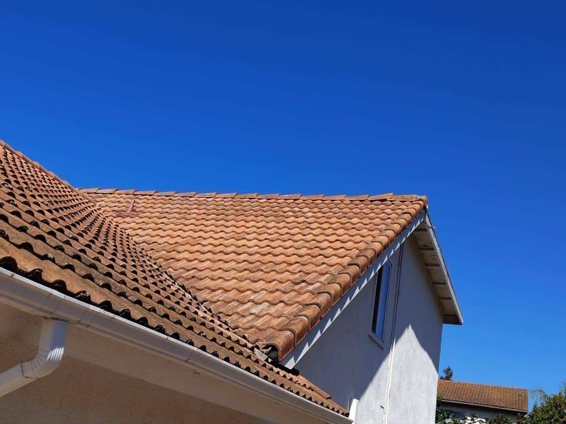 Red-tiled house roof and white wall beneath a clear blue sky