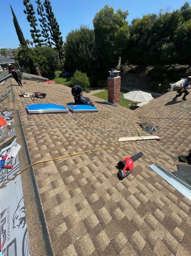 Workers installing roofing on a sloped house roof with tools and blue underlayment sheets.