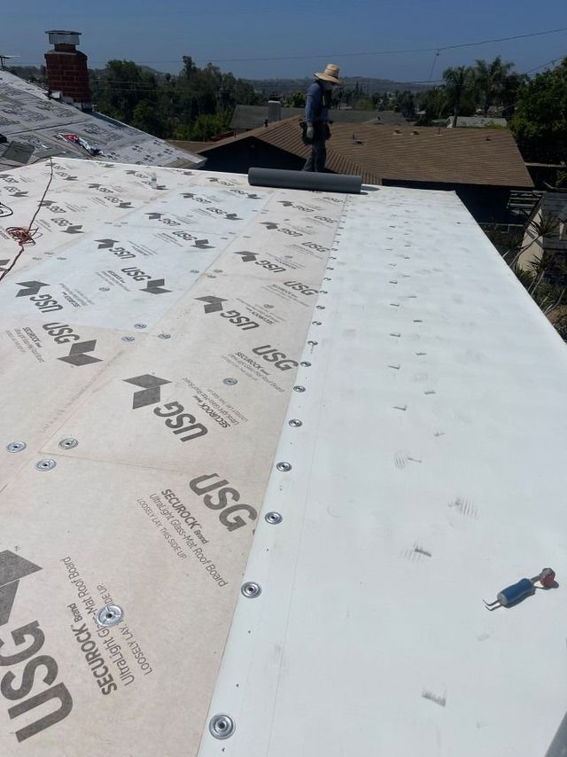 Roof under repair with white underlayment and a worker on the ridge in the background