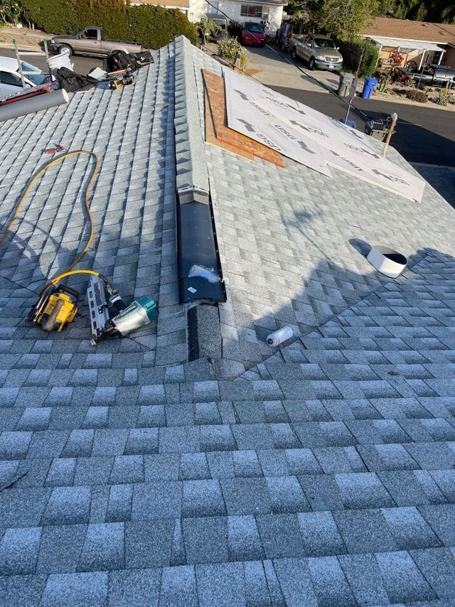 Roof under repair with shingles, tools, and exposed underlayment on a steep residential roof