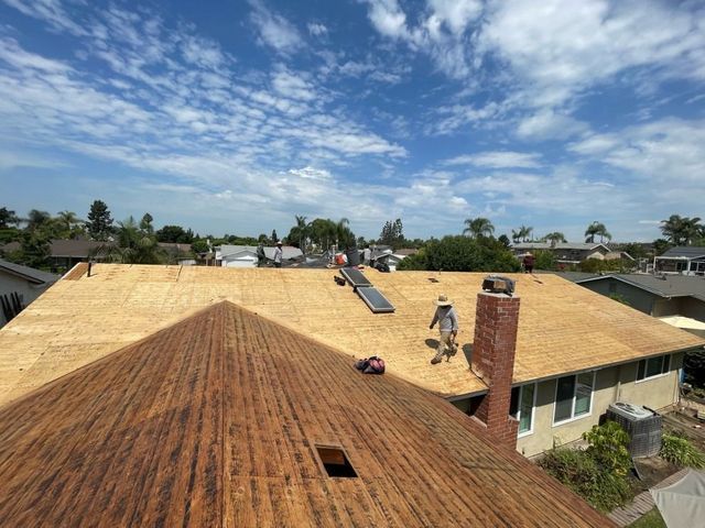 Workers repairing a rusted roof on a suburban house under a partly cloudy sky