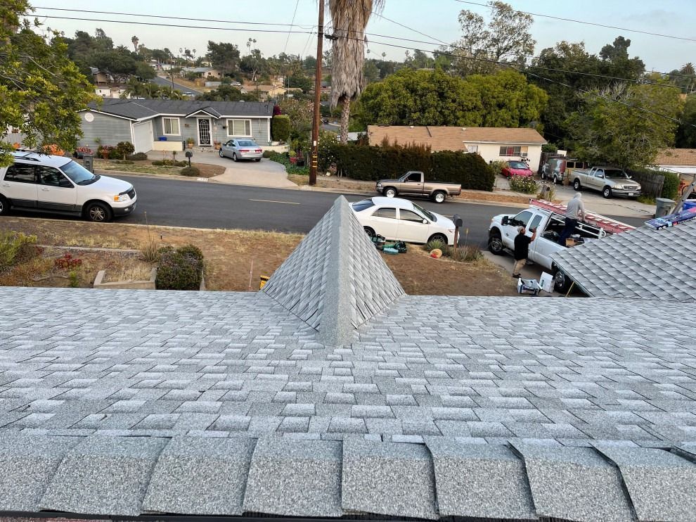 Roof shingles overlooking a suburban street with parked cars and several people near a white vehicle