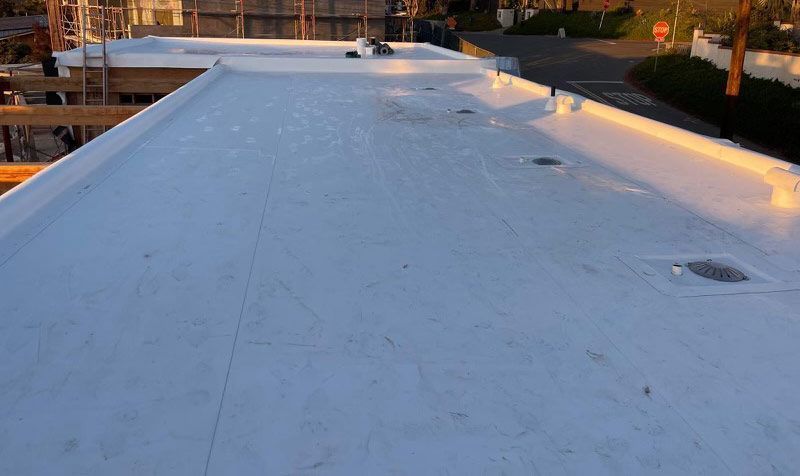 Rooftop with a white membrane surface, parapet edges, and city buildings in the background.