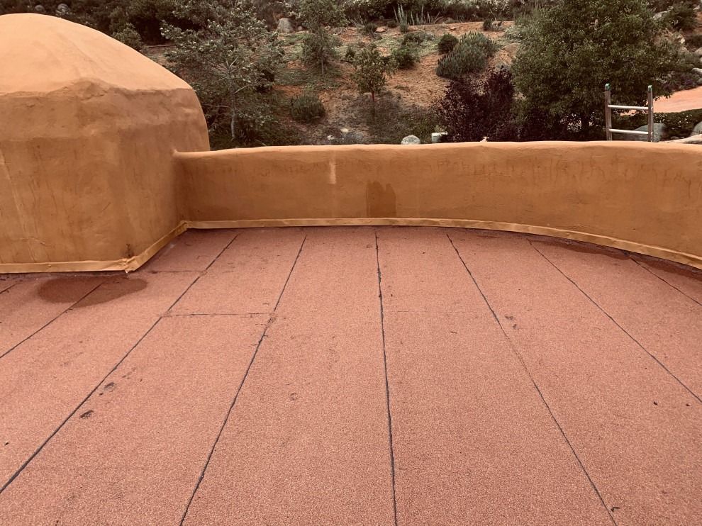 Terracotta courtyard with curved stucco wall and low parapet beside a rocky hillside.