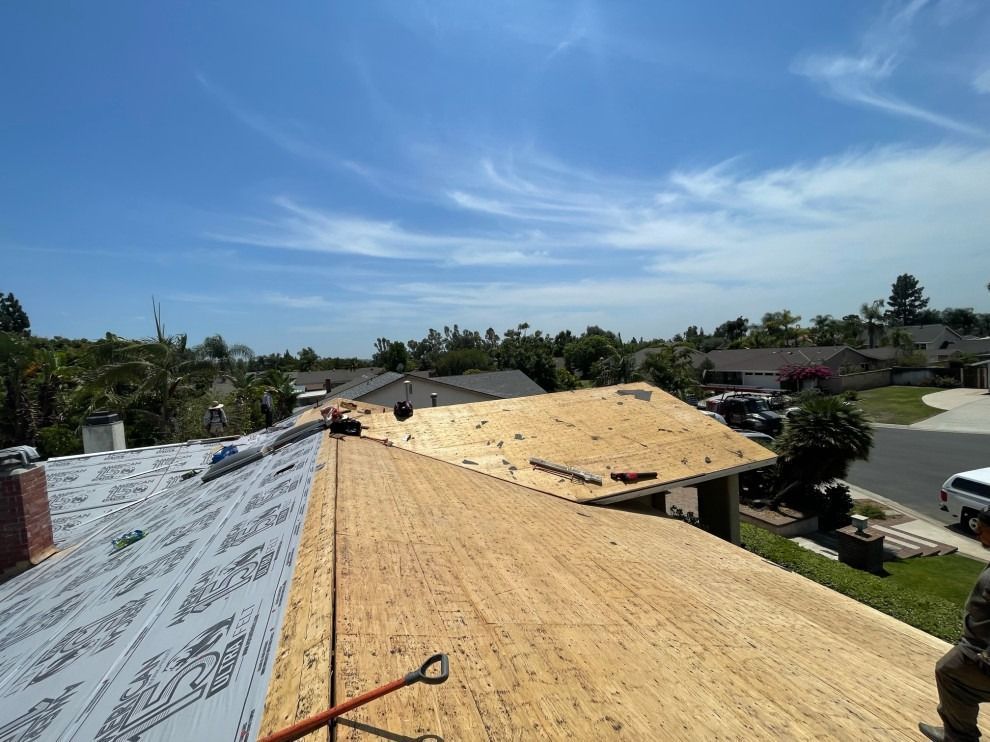 Roofers installing yellow underlayment on a suburban house roof under a clear blue sky