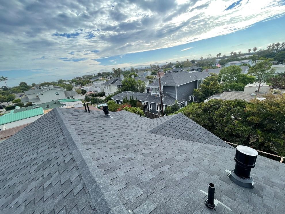 Rooftop view of suburban houses under a cloudy sky, with two people on the shingles.