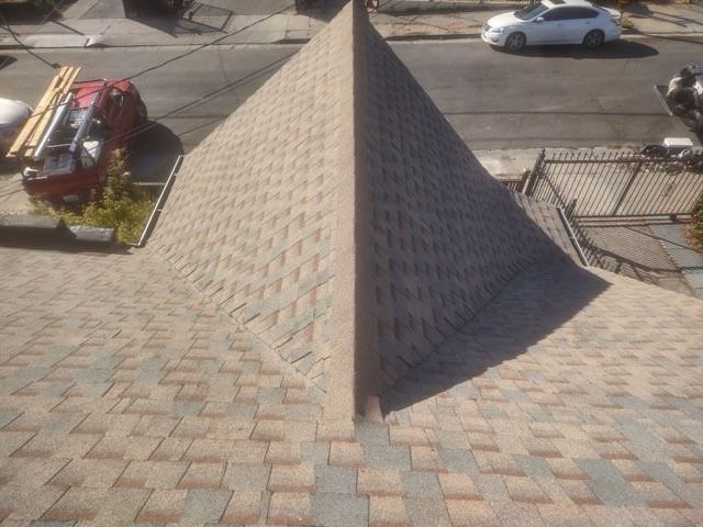 Pyramid-shaped shingled roof on a building, viewed from above, with street and parked cars nearby