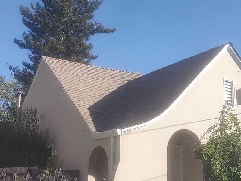 Small beige stucco house with a steep roof, arched entryways, and trees against a blue sky